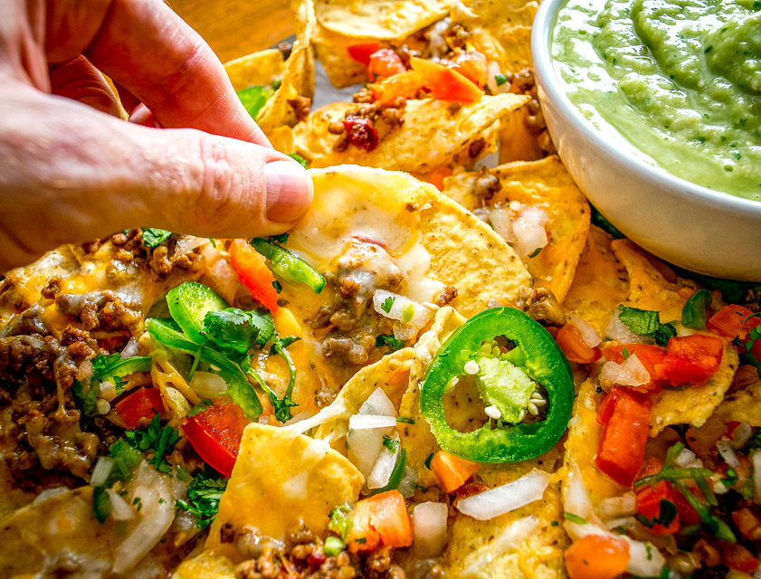 Estos Nachos picantes de carne molida tienen el potencial de salvarte el día. Los chipotles en adobo le dan a la carne un toque real y cuando se cargan en chips de tortilla cubiertos de queso, se convierten rápidamente en una comida que hay que hacer. Se sirven con una Salsa Verde de Aguacate hecha en casa y los aderezos que elijas. ¡Tan bueno! mexicanplease.com