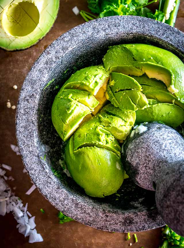 We're grinding an onion-jalapeno-cilantro paste in a molcajete for a delicious batch of homemade guacamole. Don't forget a final squeeze of lime, so good! mexicanplease.com