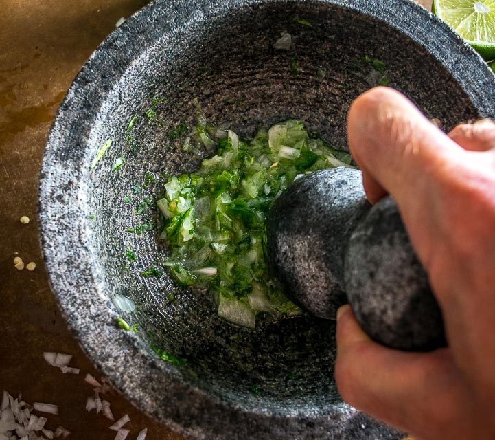 We're grinding an onion-jalapeno-cilantro paste in a molcajete for a delicious batch of homemade guacamole. Don't forget a final squeeze of lime, so good! mexicanplease.com