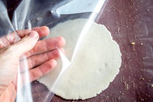Peeling plastic away from flattened dough balls.