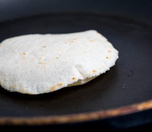 Corn tortilla puffing up in a small skillet.
