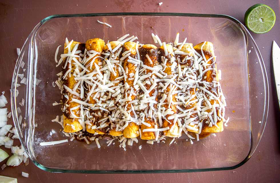 Making enchiladas in a baking dish and adding cheese.