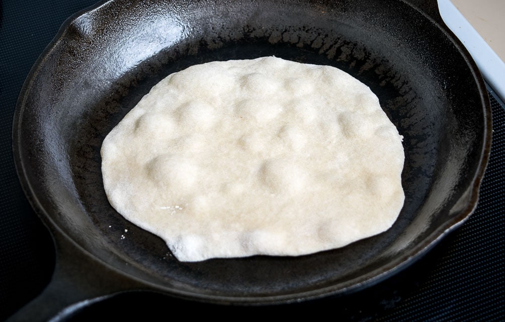 Cooking the first side of a flour tortilla until it bubbles. 