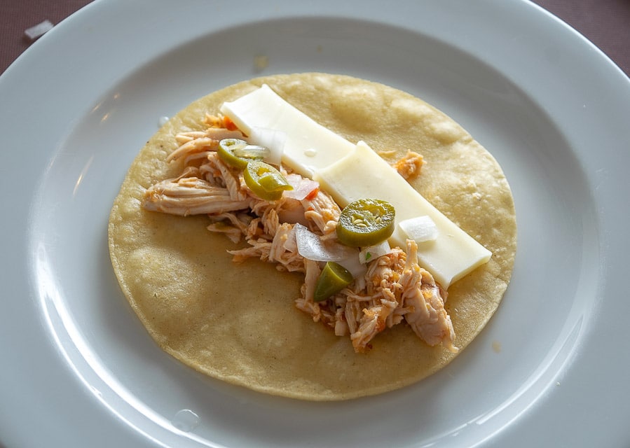 Building enchiladas with chicken, cheese, onion, and pickled serranos