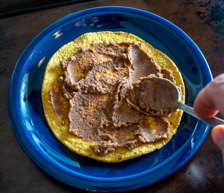 Adding refried beans to the tostadas