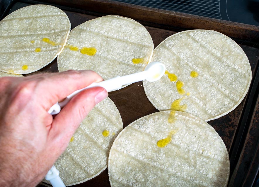 Drizzling oil on corn tortillas for homemade tostada shells