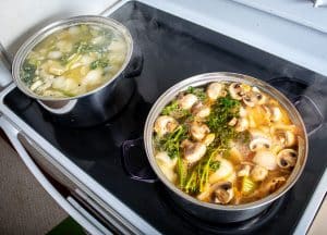 Two single gallon pots cooking different vegetable stocks