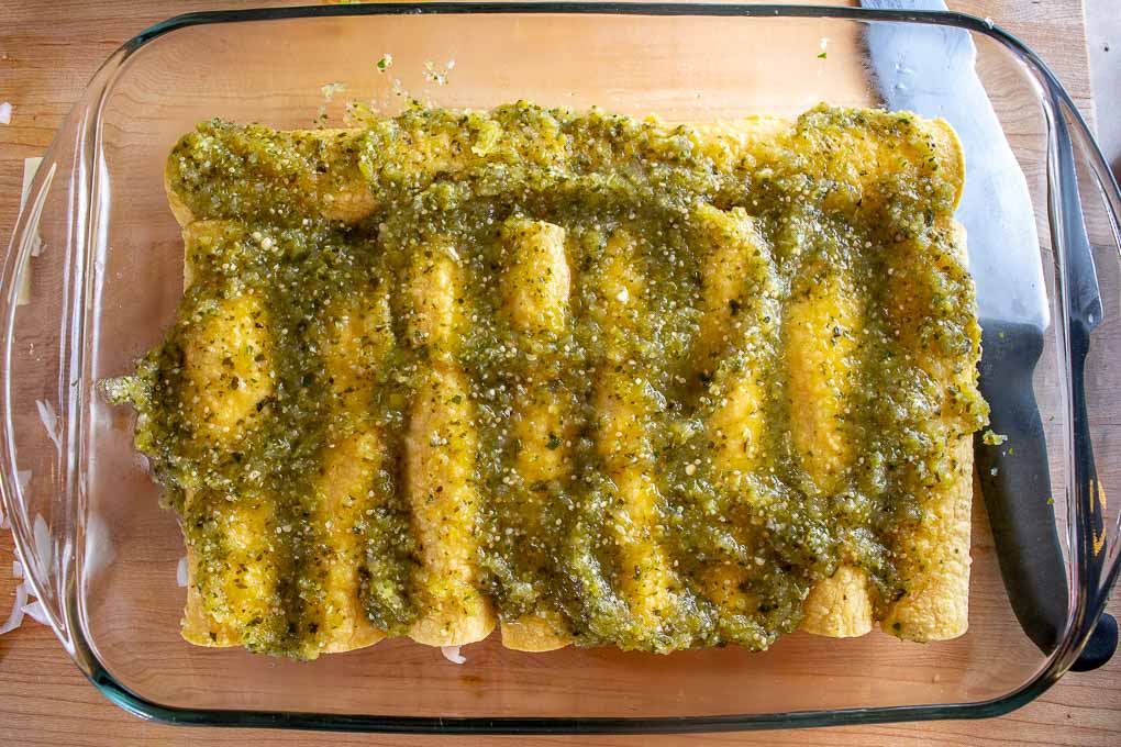 Pouring green sauce on top of enchiladas