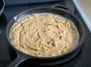 Adding cornbread mixture to a cast iron pan