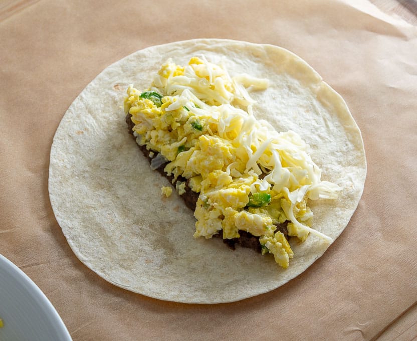 Adding beans, eggs, and cheese to the flour tortilla