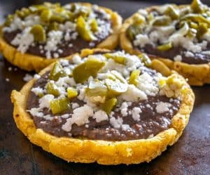 Sopes topped with pickled jalapenos, Queso Fresco, and refried beans.