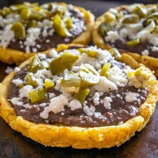 Sopes topped with pickled jalapenos, Queso Fresco, and refried beans.