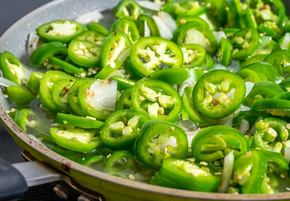 Adding sliced jalapenos to the sauce pan