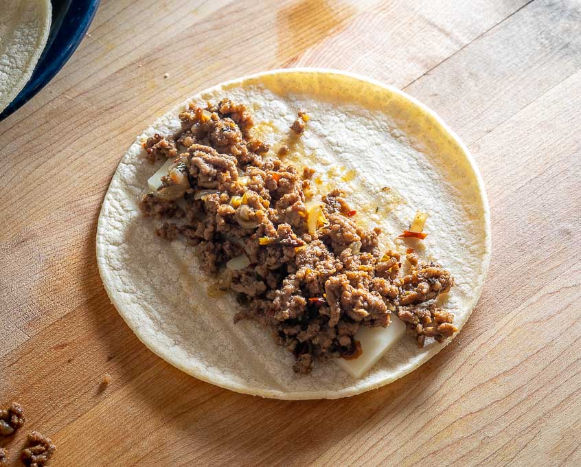Adding cheese and ground beef to the corn tortillas