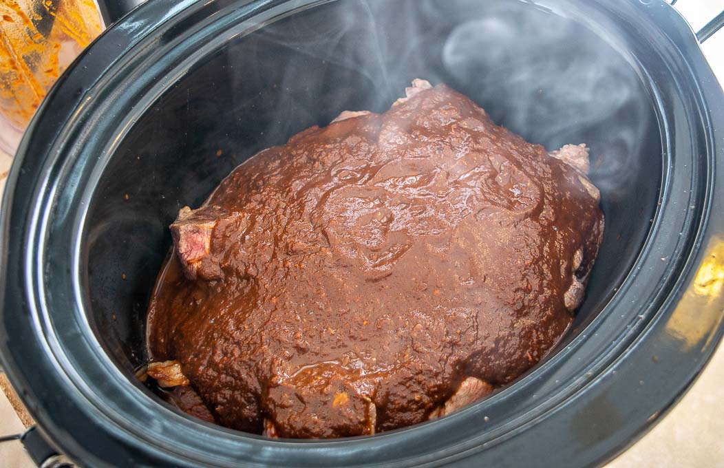 Covering beef chunks in the slow cooker with the Birria sauce
