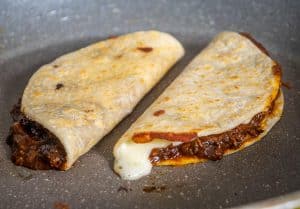 Birria tacos folded in half in the skillet