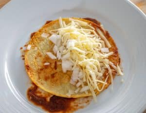 Adding shredded cheese and finely chopped raw onion to a corn tortilla