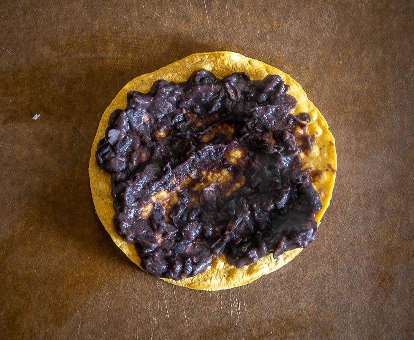 Adding refried beans to the tostada shell