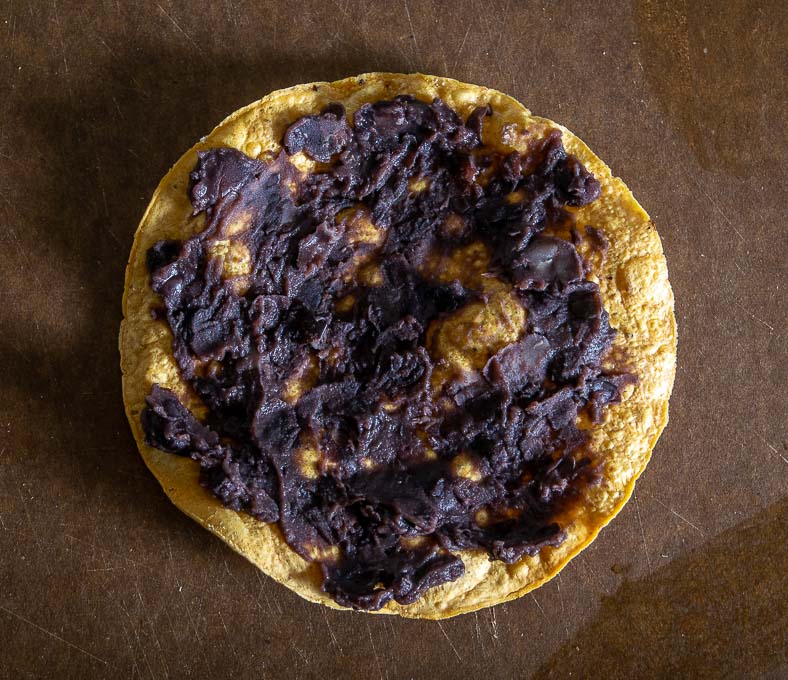 Adding a thin layer of refried beans to the tostada shell