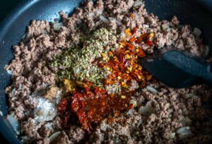 Adding cumin and Mexican oregano to the ground beef