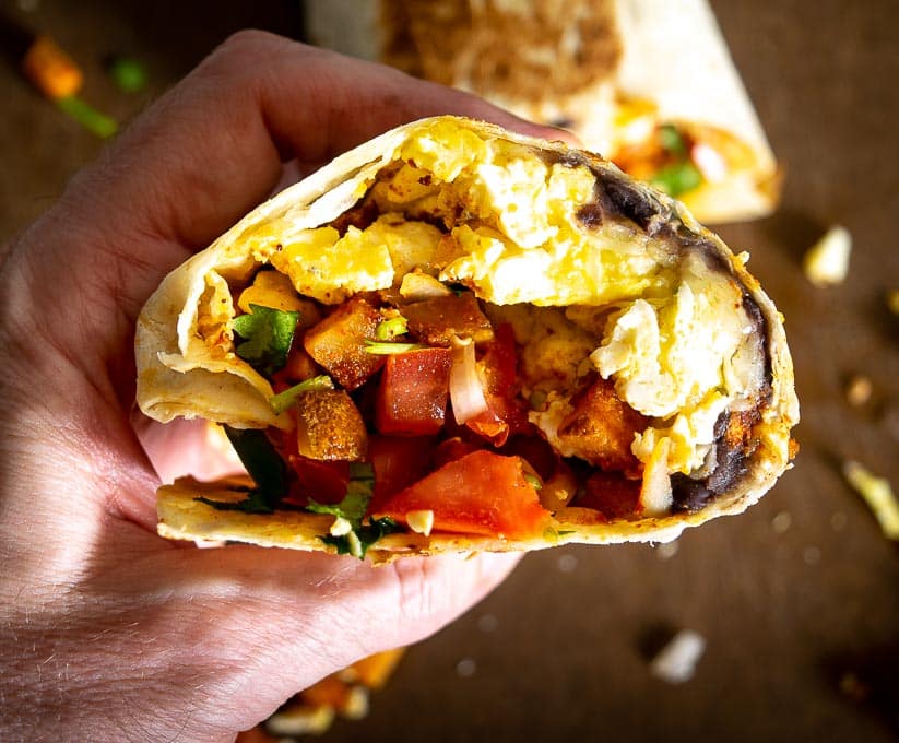 Holding breakfast burrito and taking a bite