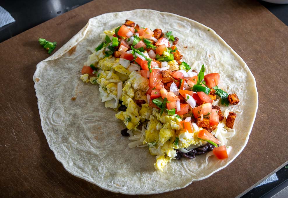 Adding eggs, Pico de Gallo, and potatoes to the breakfast burrito