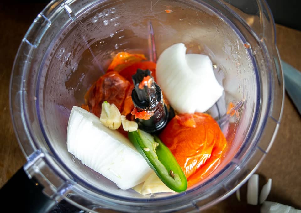 Adding ingredients to the blender for the tomato-jalapeno mixture