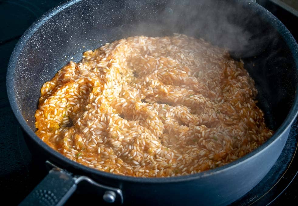 Adding tomato-jalapeno mixture from the blender to the rice