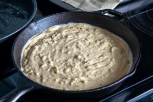 Adding cornbread batter to the pre-heated baking dish