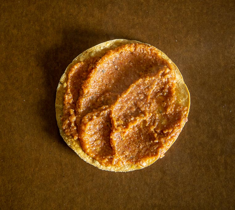 Adding Charro Bean puree to a warm tostada shell