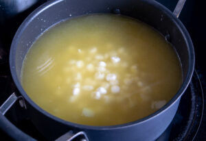 Adding hominy and vegetable stock to the pan
