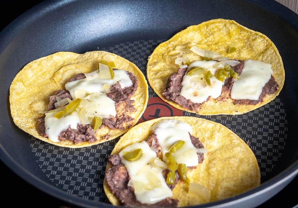 Adding refried beans, cheese, and pickled jalapenos to the corn tortillas