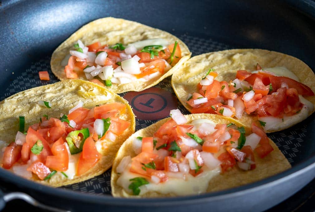 Adding cheese and Pico de Gallo to the corn tortillas