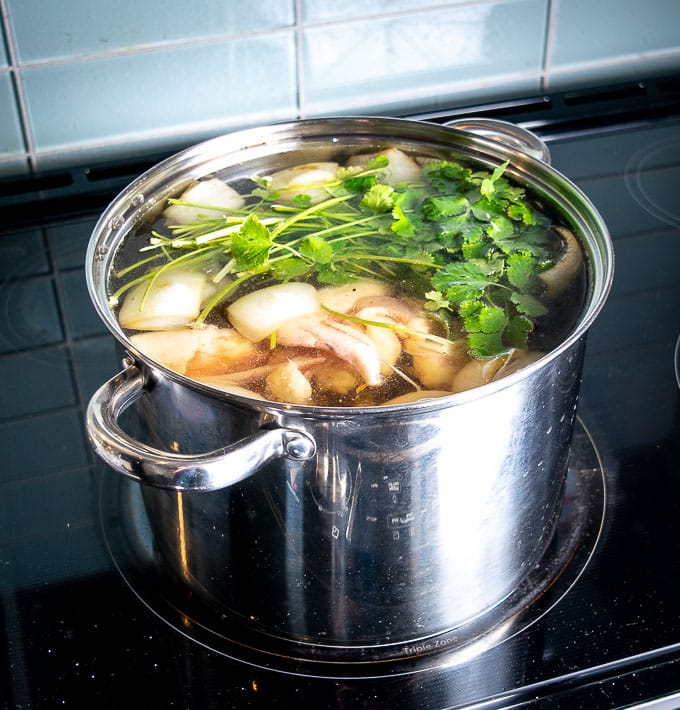 Adding cilantro and the chicken carcass to the stock