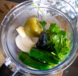Adding the ingredients for salsa verde to a blender