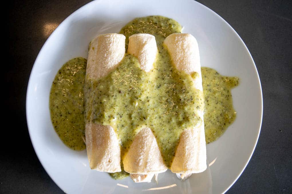 Adding three enchiladas to a plate and then coating with the creamy Poblano sauce