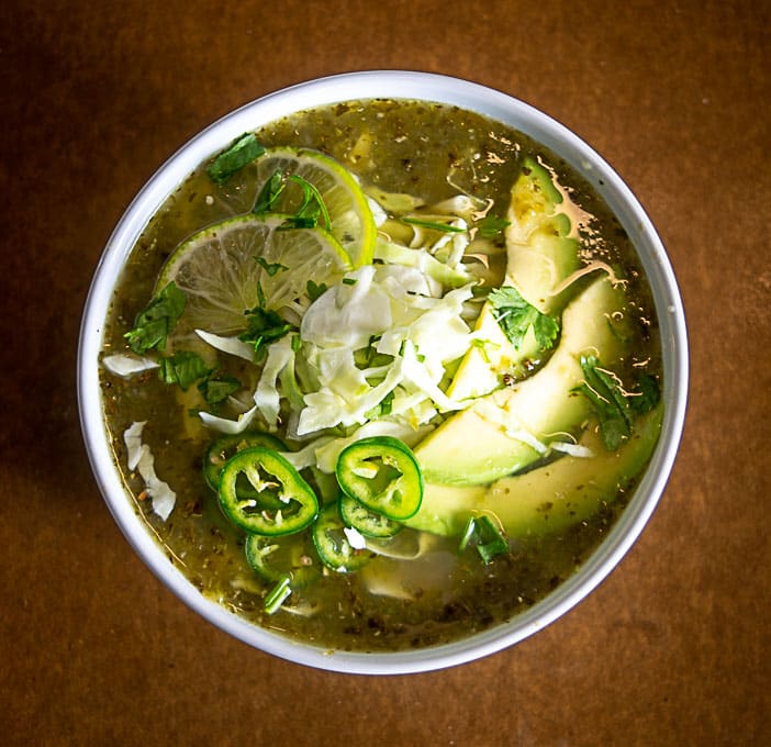 Adding cabbage, cilantro, avocado and lime to the Pozole Verde