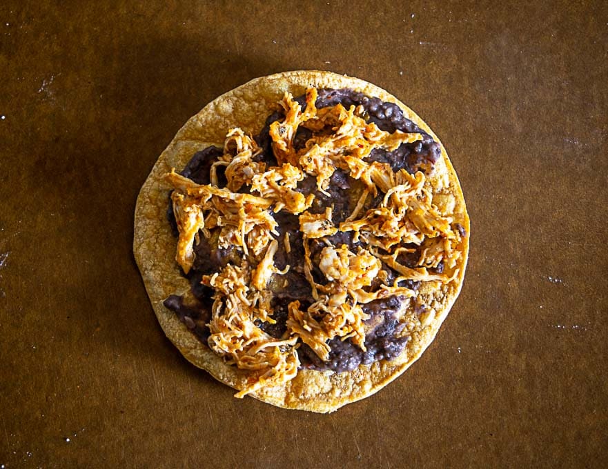 refried beans and chipotle chicken on a tostada shell