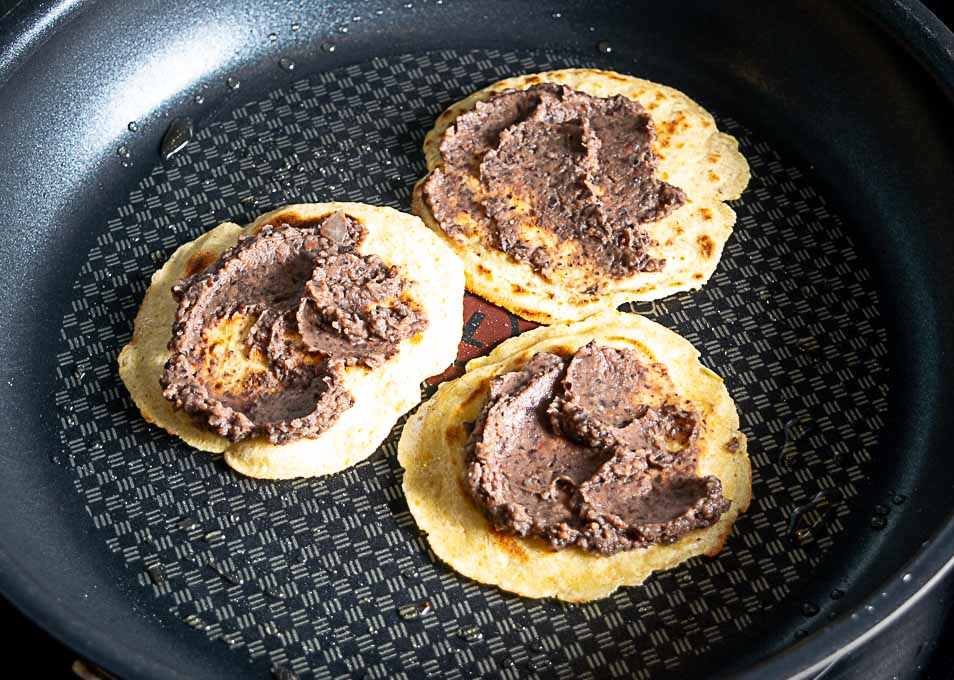 Adding beans to the tortillas in the skillet
