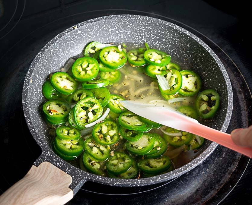 Adding the vinegar and water to the sliced jalapenos in the pan