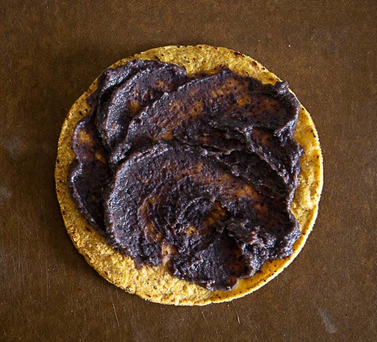 Adding thin layer of refried beans to a warm tostada shell