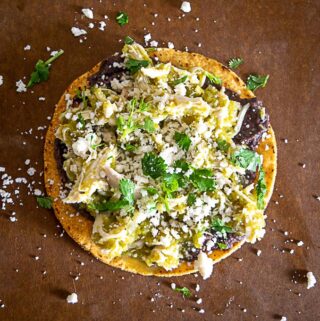 Final tostada with chicken chile verde, queso fresco, beans, cilantro, lime