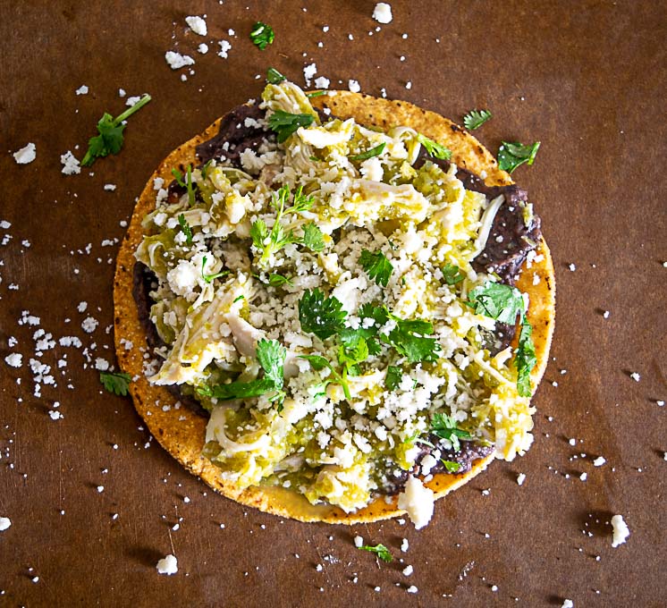 Final tostada with chicken chile verde, queso fresco, beans, cilantro, lime