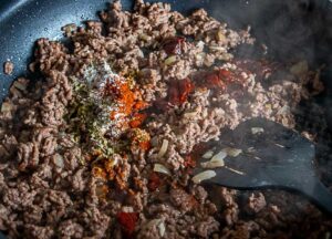 Adding chile powder and Mexican oregano to the ground beef