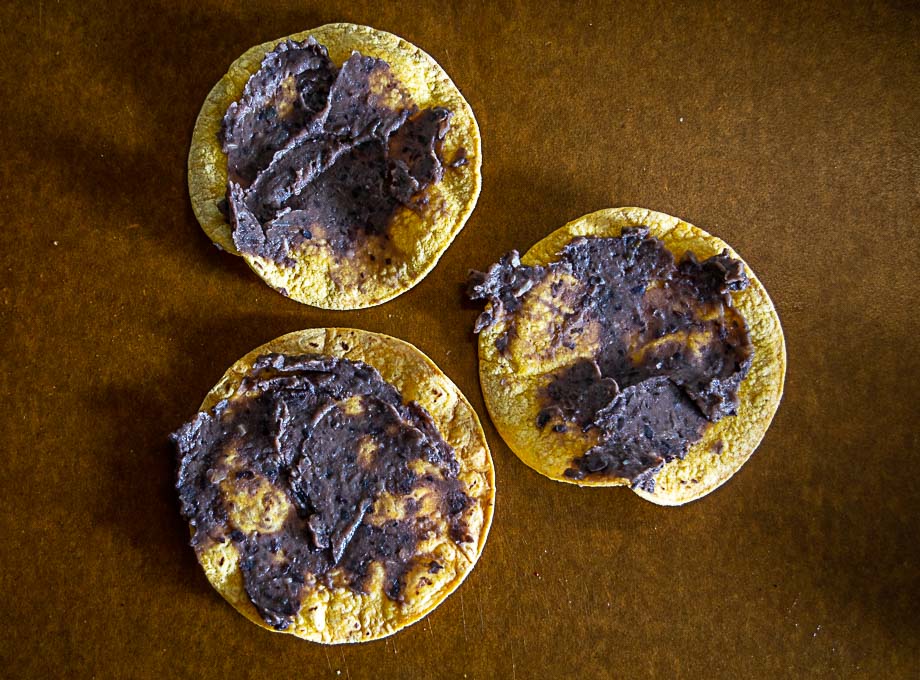 Adding thin layer of refried beans to the tostadas